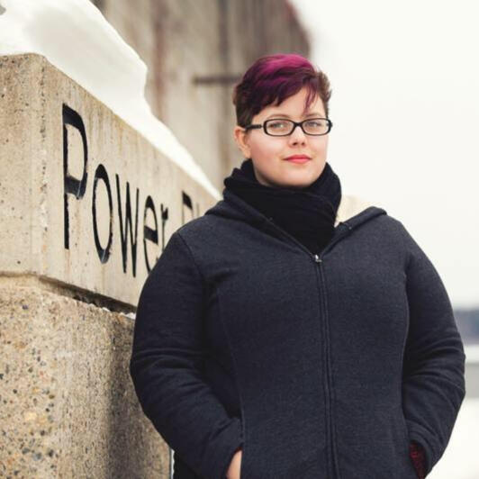 Amanda has lived all over the north. Amanda, with short violet hair, is leaning against CNC's Power Plant sign, circa 2015/6.